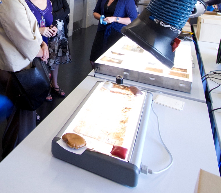 Colour photograph of light boxes on a table. Nitrate negatives are on top of the boxes. Back: Three people standing next to the table.