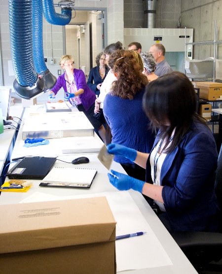 Colour photograph of workers at a nitrate work station. Front: A female employee handling a nitrate negative; Back: A group of people discussing another nitrate negative.