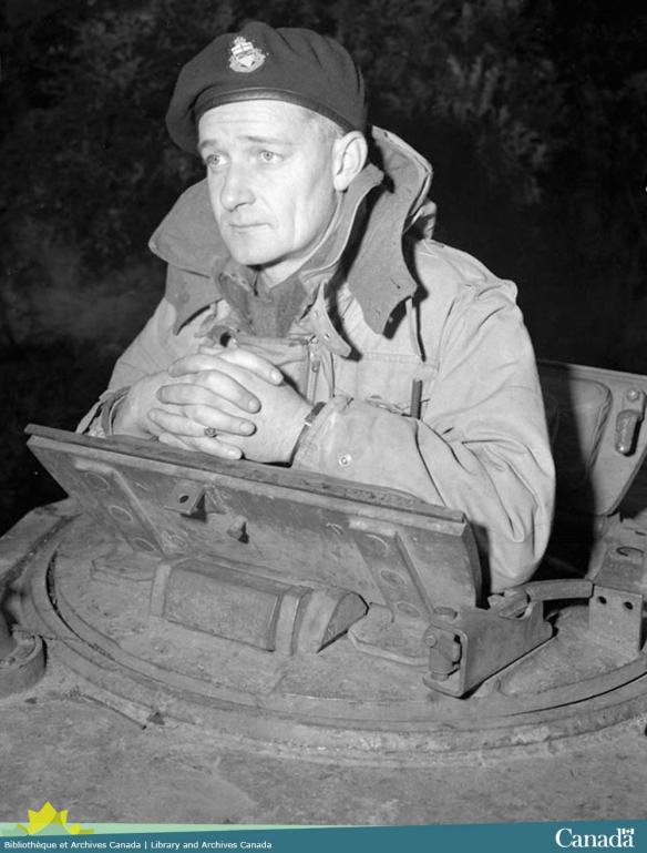 Black and white photograph showing a man peering out over a tank turret.