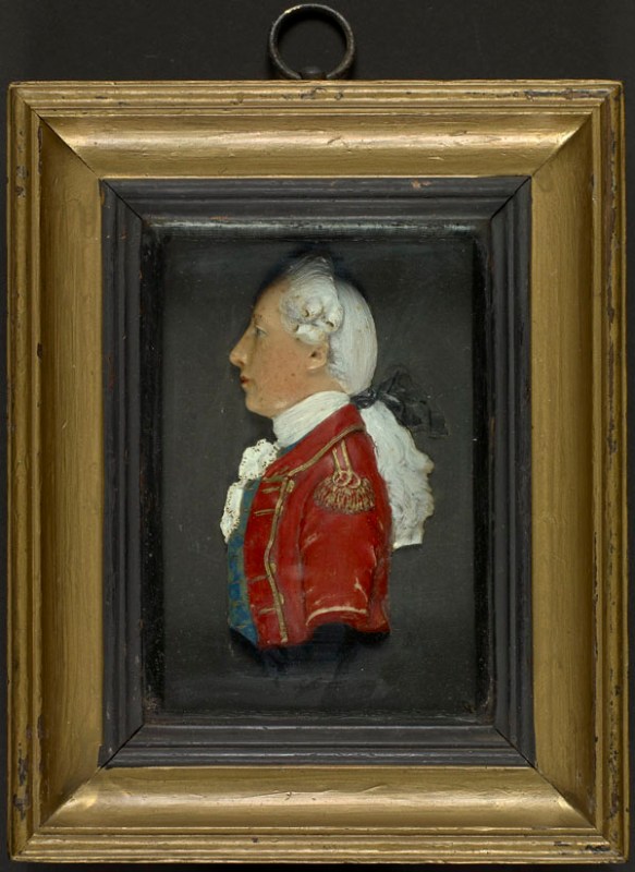 Wax miniature, by an anonymous artist, early 19th century. This rather generic wax miniature shows a man in profile wearing a red British coat embellished with gold trimming, a white cravat and a blue waistcoat. He has long white hair, tied back. The miniature is quite sculptural.