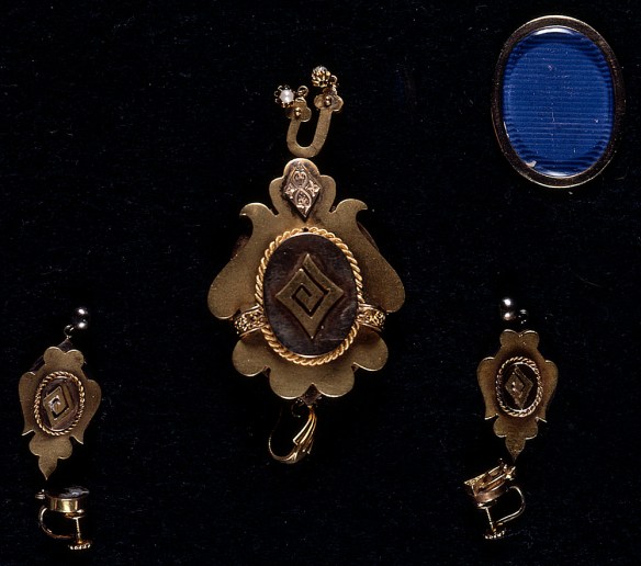 Colour photograph of two gold earrings with a stylized spiral pattern and a matching pendant.