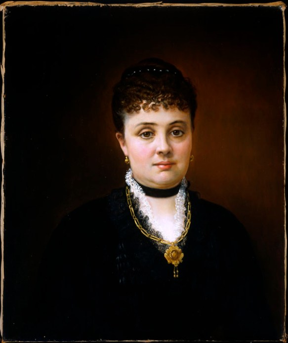 Oil painting showing a woman in a black dress looking straight at the viewer. She is wearing the same pendant and earrings as shown in the previous photograph.