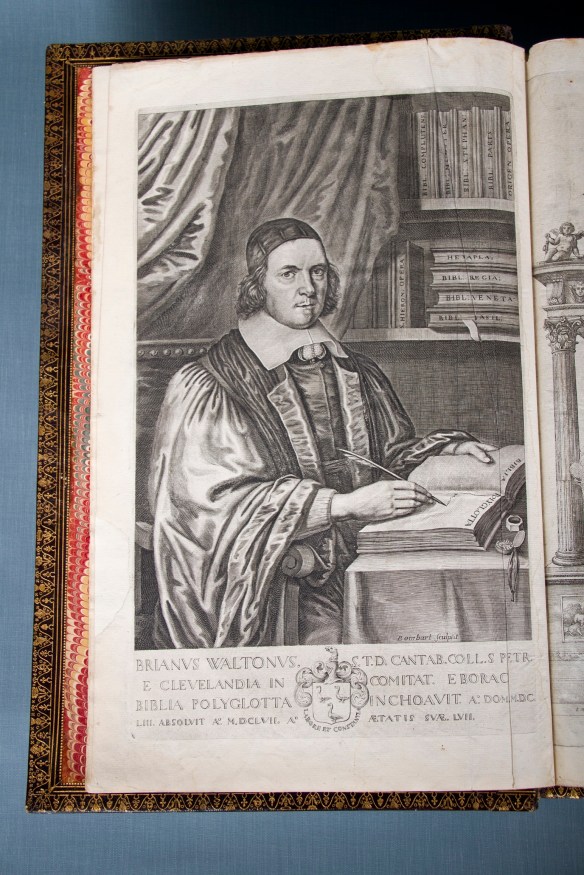 Colour photograph showing an image of a man standing in bishop’s robes with a quill in his hand and looking directly at the reader.