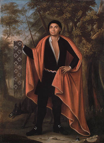 Oil painting on canvas showing a man standing in a forest with a wolf at his feet. He is dressed in black, wearing a red cape, and holding a wampum belt in his hand.