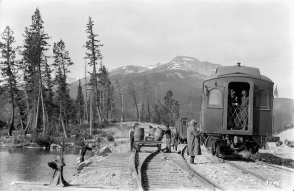 A black-and-white photograph showing a train stopped beside a river.
