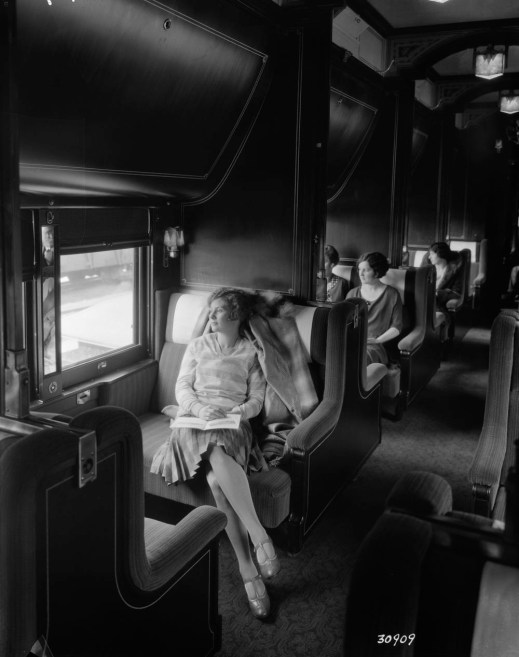 A black-and-white photograph of people seated in a railway sleeping car, looking out the windows.