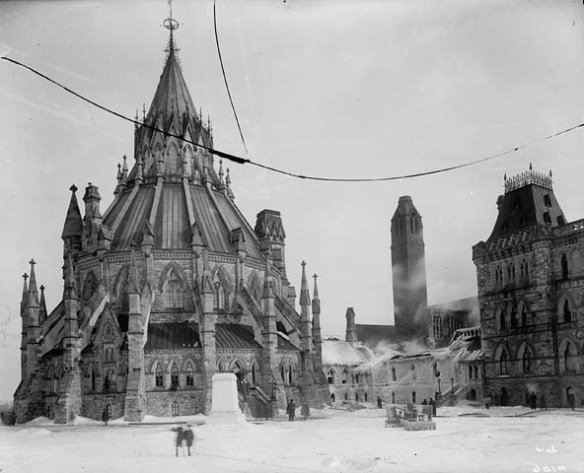 A black-and-white photograph showing a very elaborate round building with pinnacles and flying buttresses in a wintry setting next to a building partly encased in ice. Firemen are putting out a fire.