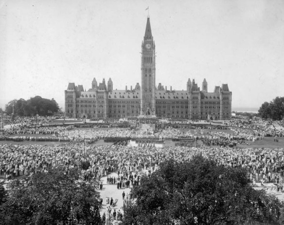 A black-and-white photograph showing the main Parliament building from the front with crowds of people filling Parliament Hill.