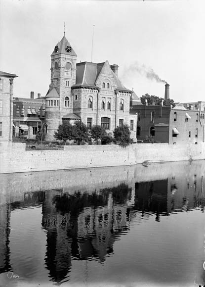 A black-and-white photograph of a castle-like building overlooking a waterway, very similar to a moat.