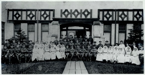 A black-and-white photograph of uniformed men and nurses seated in front of an elaborate Elizabethan entrance.