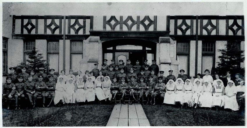 A black-and-white photograph of uniformed men and nurses seated in front of an elaborate Elizabethan entrance.