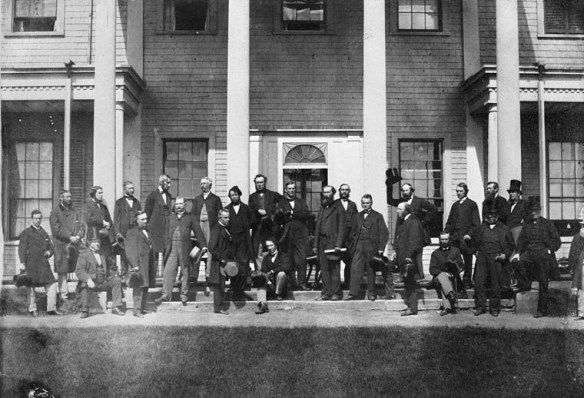 A black-and-white photograph of a group of men standing in front of a building.