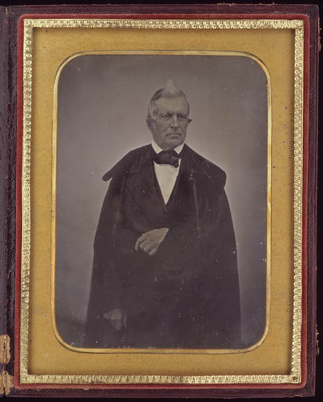 A colour photograph of a black and white image in a gold frame showing a man in an evening cape. The image looks hazy and dull.