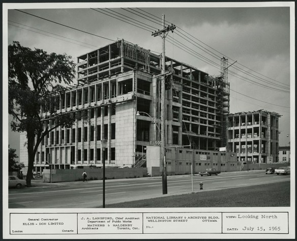 A black-and-white photograph showing the unfinished facade of a 10-storey building. There is construction board on the ground floor. There are cars (including a VW bug!) and pedestrians going about their business.