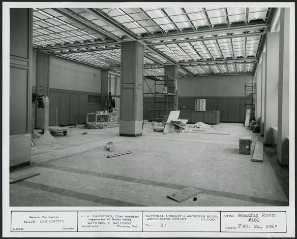 A black-and-white photograph of a large room with scaffolding and construction materials scattered about. 