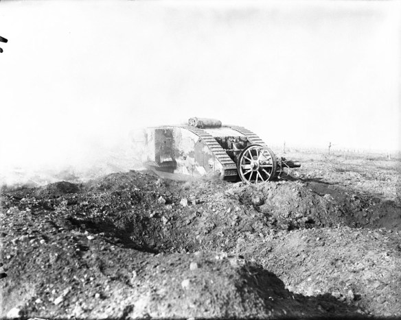 A black-and-white photograph of a British heavy tank advancing through a shell-cratered landscape.
