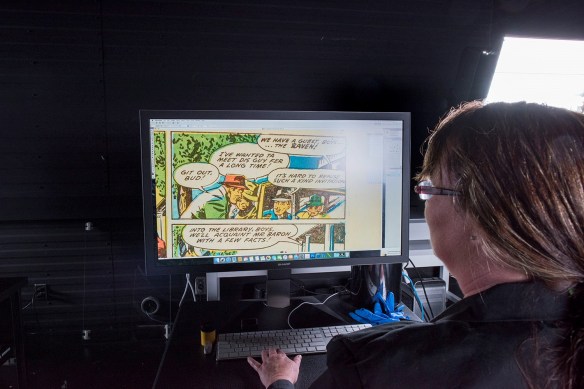A woman faces a computer monitor showing an image of a page from a comic book.