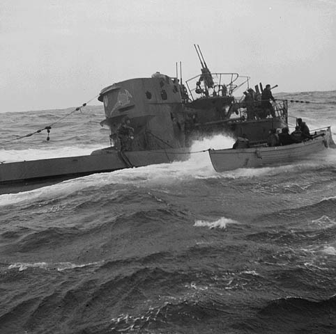 Black-and-white photograph showing a submarine and a whaler side by side. Members of the submarine’s crew can be seen on the bridge. The people in the whaler are seated.