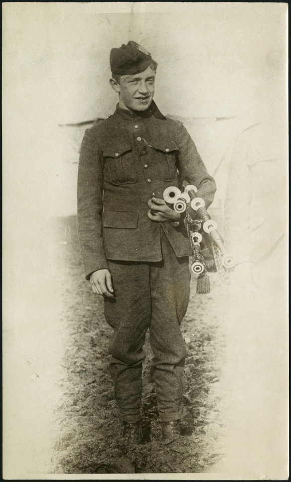 Black-and-white photograph of a young man in military uniform holding his bagpipes.