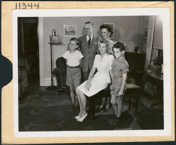 A black-and-white photograph of a family group, including a woman, man and three children in a living room.