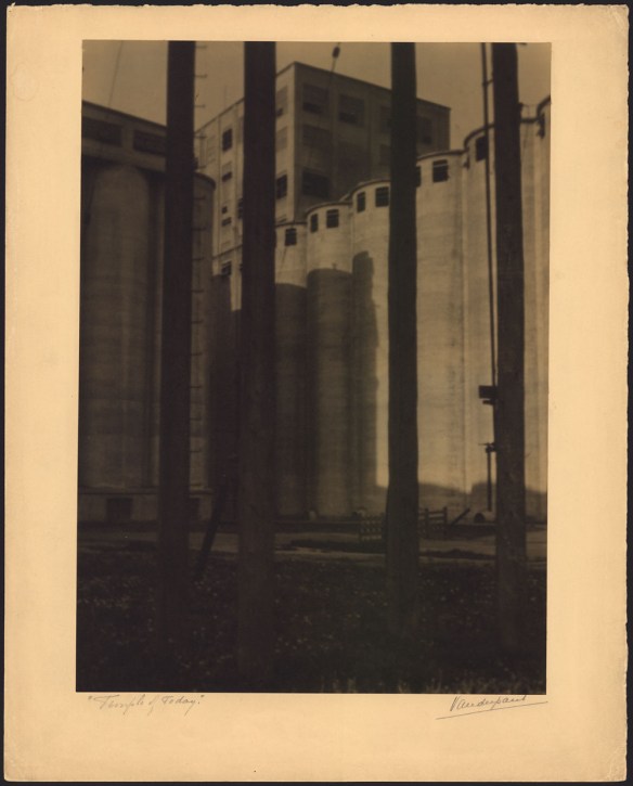 Black-and-white photo of a grain elevator with tall, circular towers in front of a taller rectangular building.
