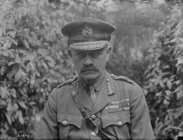 A black-and-white photo of a uniformed man with a moustache, wearing an officer’s cap and a Sam Browne belt. His tunic is festooned with medals and military decorations, and he is staring directly and impassively into the camera.