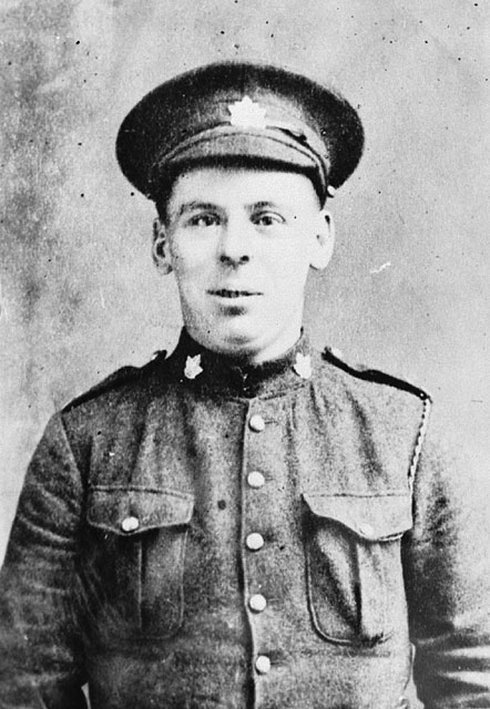 A black-and-white photograph of a man in uniform. His cap and collar are adorned with maple leaves, and he is looking directly at the photographer. 
