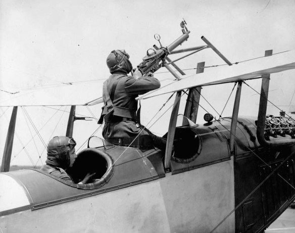 A black-and-white photograph of a biplane with two aviators in the cockpits: one is piloting and the other is at the machine gun.