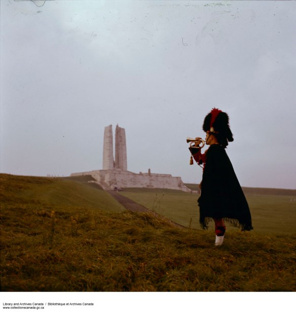 A colour photograph of a bugler in Highland uniform in front of the Vimy Ridge memorial.