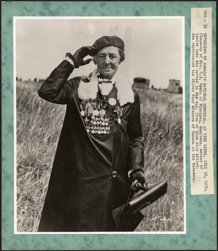 A black-and-white photograph of a woman saluting wearing a beret and coat with many medals pinned upon it.