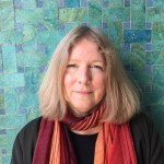 Colour photograph of a woman standing against a turquoise tiled wall.