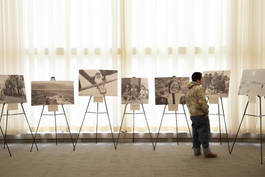 A colour photograph of a young Inuit man looking at several large photographs on easels. 
