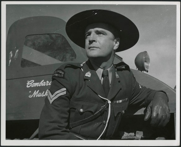Black-and-white still of an actor in an RCMP uniform leaning against a Bombardier truck.
