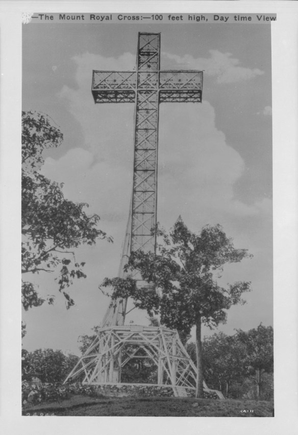 A black-and-white photograph showing a large metal cross with the text, “The Mount Royal Cross—100 feet high, daytime view.”
