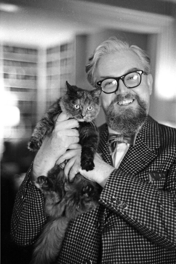 A black-and-white photograph of a man smiling while holding a cat near his shoulder.
