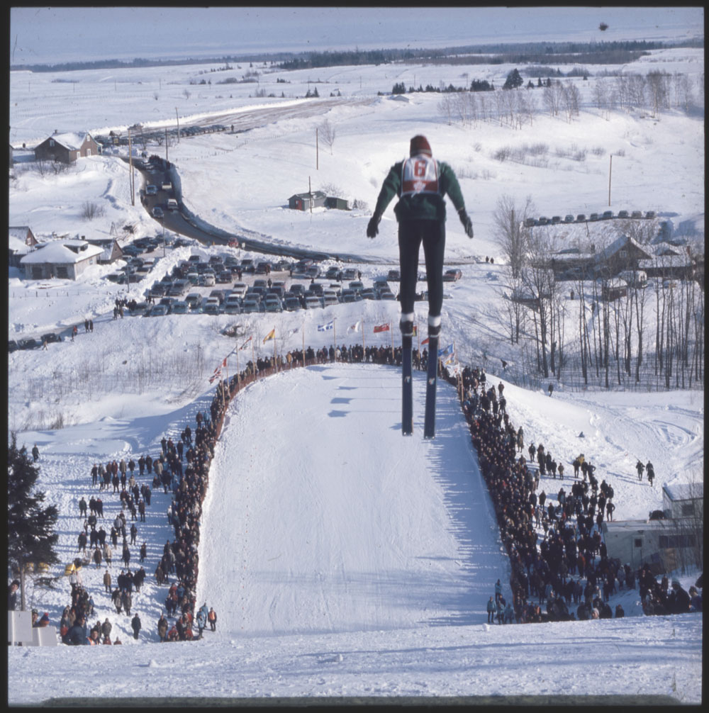 A colour photograph of a ski jumper flying above a crowd of spectators.