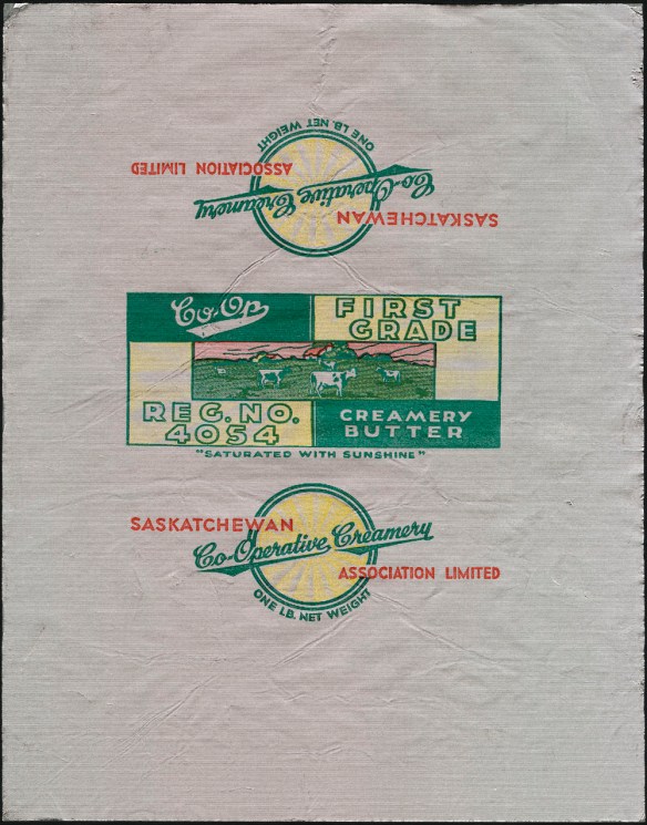 A colour printed foil wrapper with an image of cows grazing in a meadow. The text reads: “Co-op. First Grade. Creamery Butter. Reg. No. 4054.” One of the other sides has the following text: “Saskatchewan Co-Operative Creamery Association Limited. One lb net weight.”