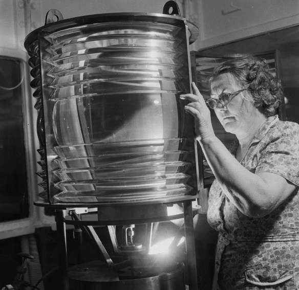A black-and-white photograph of Eliza Campbell examining a lighthouse lamp.