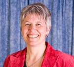 Colour photograph of a woman with short hair and wearing a crimson blazer smiling.