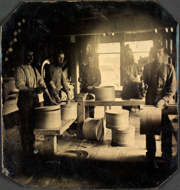 A black-and-white photograph of five men assembling wooden boxes inside a mill.