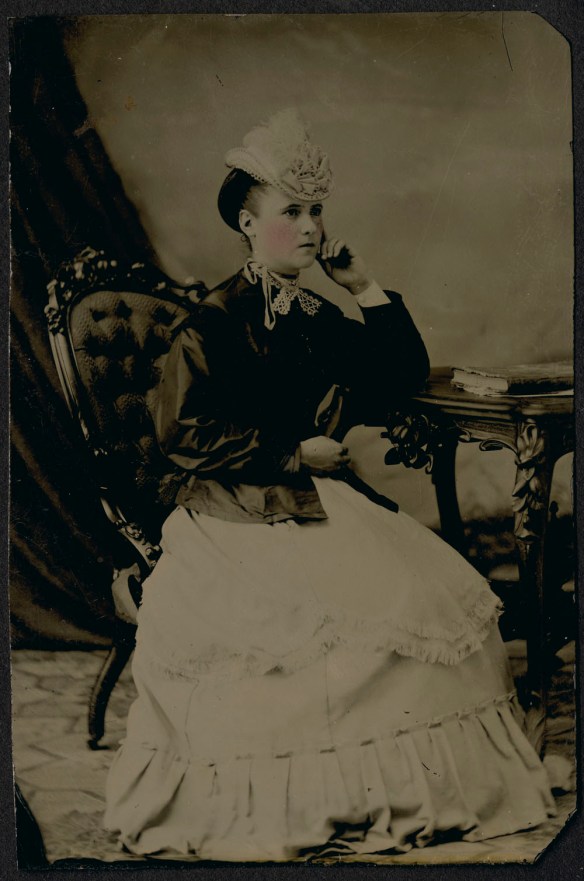 A hand-tinted, black-and-white portrait of a seated woman.