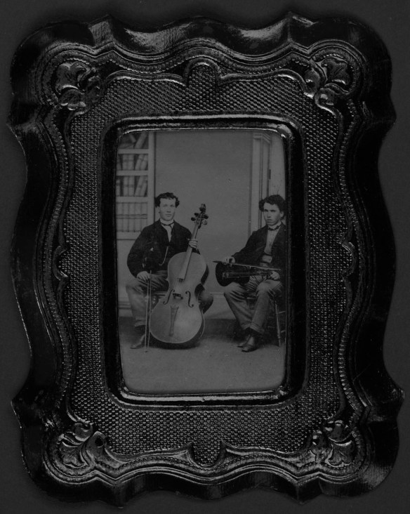 A black-and-white portrait of two young men seated. One is holding a violin and the other is holding a cello.