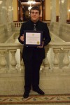 A colour photograph of a young man standing with a diploma.