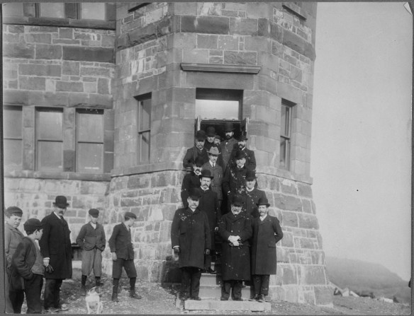 A black-and-white photograph of Guglielmo Marconi posing on the steps of a building with 12 members of the administration of Newfoundland, Signal Hill, St. John's.