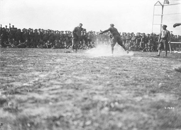 A black-and-white photograph of a player sliding into home plate. The catcher is standing over the base while the umpire makes the call. A crowd of soldiers cheers them on. 
