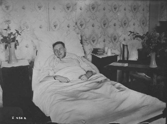 A black-and-white photograph of a smiling young man lying in bed.