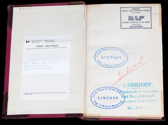 A colour photograph of the front endpapers of an open book showing a bookplate on the left-hand page and four stamps on the right-hand page.