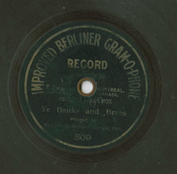 A colour photograph of a record label that reads “Improved Berliner Gram-O-Phone Record. Manufactured by [illegible] Montreal, Canada. Patented [illegible] 1897. Ye Banks and Braes. Played by The Kilties Band – Belleville, Ont.”