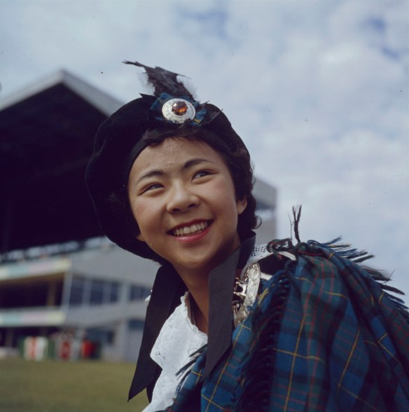 A colour photograph of a smiling girl wearing a tam and tartan shoulder accessory. 