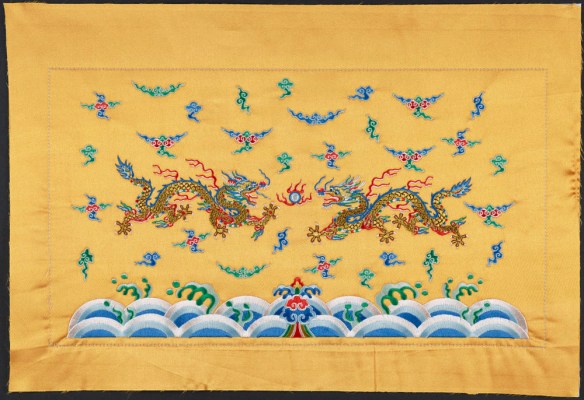 An embroidered golden cloth of two dragons reaching for a pearl and flying amongst clouds with ocean waves rolling below them.